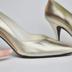 May include: A pair of gold-colored high heels with pointed toes and stiletto heels. The shoes have a metallic sheen and a classic design, suitable for formal occasions. The heels are approximately 3 inches tall.