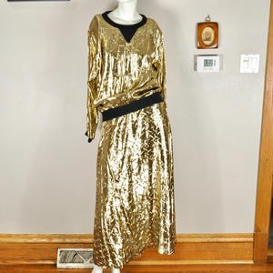 May include: A gold sequined dress with long sleeves and a midi-length skirt. The dress features a black neckline and a black band at the waist. The dress is displayed on a mannequin.