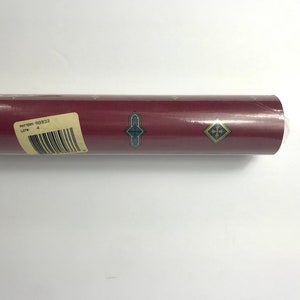 Può includere: Un rotolo di carta da parati bordeaux con un motivo geometrico dorato e blu. L'etichetta sul rotolo riporta "Modello: RG933 Lotto: 4".