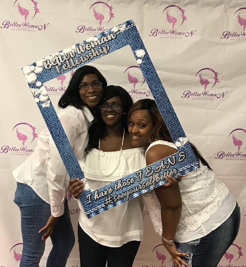 May include: Three women are posing for a photo with a blue denim photo booth prop. The prop has the text "Better Woman Fellowship" and "I have those JEANS #seeyourselfbetter".