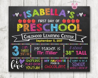 May include: A colorful chalkboard sign announcing Isabella's first day of preschool. The sign includes details about her age, height, favorite things, and teacher. It features a chalkboard background with colorful text and illustrations.