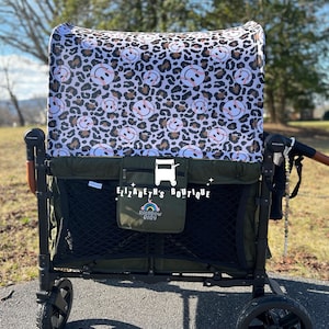 May include: A green utility wagon with black wheels and a canopy featuring a pattern of baseballs with smiley faces and leopard print. The wagon has a black mesh interior and a small green pouch with the text "Elizabeth's Boutique" and "Rainbow Baby".