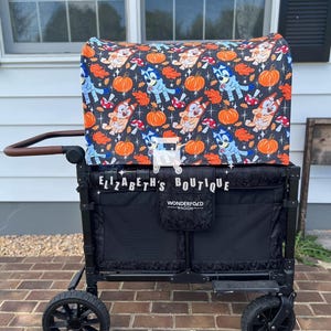 May include: A black wagon with a removable canopy featuring a fall-themed pattern with blue and orange cartoon dogs, pumpkins, and leaves. The canopy has the text "Elizabeth's Boutique" on the side. The wagon has the text "Wonderfold Wagon" on the side.
