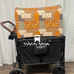 Op de afbeelding: Een zwarte wagen met een patchwork stoffen kap in tinten oranje, bruin en wit. De wagen heeft een Wonderfold logo en de tekst "Elizabeth's Boutique".