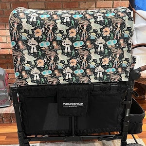 Könnte beinhalten: Schwarzer Wagen mit einer schwarzen und weißen gemusterten Stoffabdeckung mit Figuren aus dem Toy Story-Film-Franchise. Der Wagen hat zwei große Räder und ein Wonderfold Wagon-Logo auf der Vorderseite.