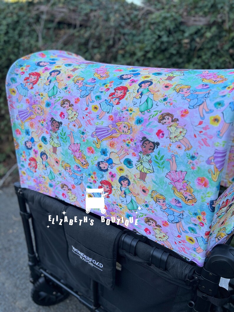 May include: A black wagon with a white and purple fabric canopy featuring a pattern of Disney princesses. The canopy has the text "Elizabeth's Boutique" printed on it. The wagon has a black Wonderfold Wagon logo on the side.