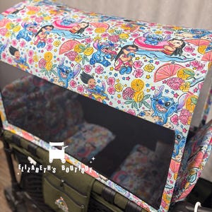 May include: A wagon canopy with a blue, pink and yellow print featuring Stitch and other Disney characters. The canopy is made of a lightweight fabric and has a clear window. The wagon is green and has a black mesh basket.
