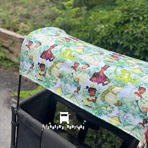 May include: A black Wonderfold wagon with a canopy featuring a whimsical print of cartoon characters in shades of green, white, and brown. The canopy is decorated with images of a princess, a frog, and an alligator. The text "Elizabeth's Boutique" is visible.