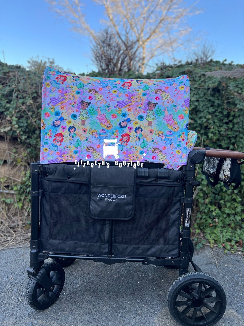 May include: A black wagon with a canopy featuring a colorful print of Disney princesses. The canopy is labeled "Elizabeth's Boutique". The wagon has a black Wonderfold label and a black mesh storage area.