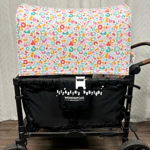May include: A black wagon with a white canopy featuring a colourful abstract leopard print. The canopy is labelled "Elizabeth's Boutique" and "Wonderfold Wagon".