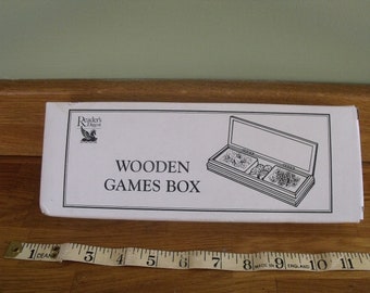 May include: A white box with the words "Wooden Games Box" printed on it. The box is from Reader's Digest and features a black and white illustration of a wooden box with compartments for games.