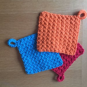 May include: Three crocheted pot holders with loops. One is orange, one is blue, and one is red.