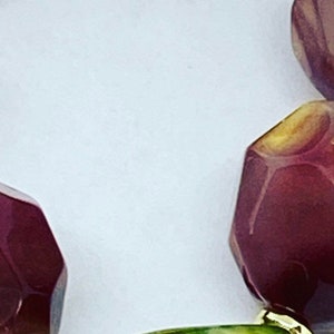 Puede incluir: Primer plano de una cuenta de piedra de ágata verde, blanca y marrón con detalles dorados. La cuenta es parte de un collar de piedras preciosas multicolores.
