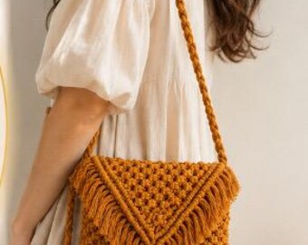 May include: Mustard yellow macrame crossbody bag with a woven pattern and fringe detail. The bag has a long, braided strap. The bag is a stylish accessory.