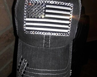 May include: A black and gray trucker hat with a distressed denim look. The hat features a rhinestone-encrusted American flag design on the front.