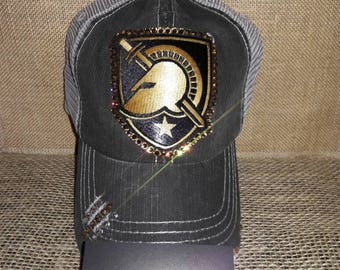 May include: A black and gray trucker hat with a gold and black embroidered patch of a Spartan helmet and sword. The patch is embellished with rhinestones. The hat has a distressed look with rhinestones on the brim.