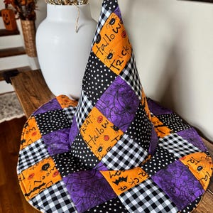 May include: A patchwork witch hat featuring a conical shape and wide brim, constructed from fabric squares in orange, purple, black, and white. Patterns include black and white buffalo check, black with white stars, and orange with text reading Trick or Treat.