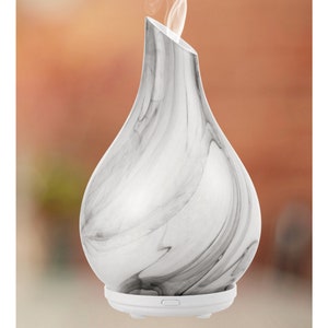 May include: White ceramic essential oil diffuser with a marble pattern. The diffuser has a pear-shaped body and a round base with a button.