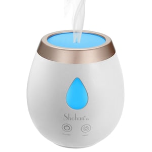 May include: White oval-shaped essential oil diffuser with a gold top and a blue light. The diffuser has a blue water drop icon and the text "Shohan" and "kv" on the front. The diffuser has two buttons: "ON/OFF" and "LIGHT".