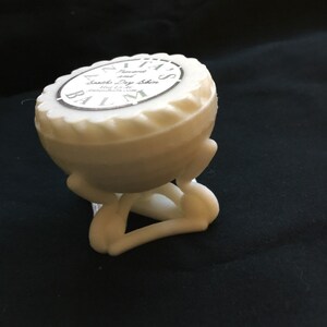 May include: White ceramic container with a round top and three legs. The container has a label that reads "Anita's  Lavender  Smooth Dry Skin Balm  1 oz.  Handmade in the USA."