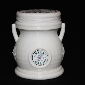 May include: White ceramic jar with a lid and two handles. The jar has a green and white label with the text "Anita's Balm".