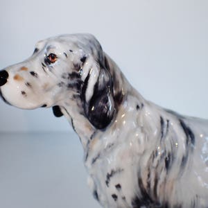 May include: A ceramic figurine of a white and black English Setter dog. The dog is standing with its head turned to the side and its ears perked up.