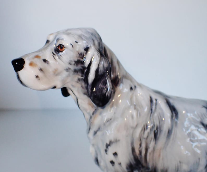May include: A ceramic figurine of a white and black English Setter dog. The dog is standing with its head turned to the side and its ears perked up.