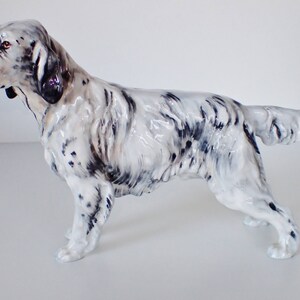 May include: A white and black porcelain figurine of a standing English Setter dog. The dog is posed with its head turned to the left and its tail curled.