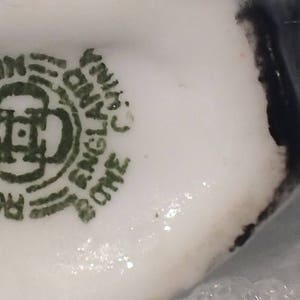 May include: Close-up of a white porcelain teacup with a green and black mark that reads "Royal Doulton, Made in England, One England China, Fine Bone China".