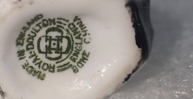May include: Close-up of a white porcelain teacup with a green and black mark that reads "Royal Doulton, Made in England, One England China, Fine Bone China".