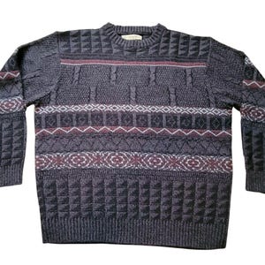 May include: A gray sweater with a crew neck and long sleeves. The sweater features geometric and patterned designs in shades of gray, burgundy, and white. The sleeves and body have different textured patterns. A classic, warm garment.