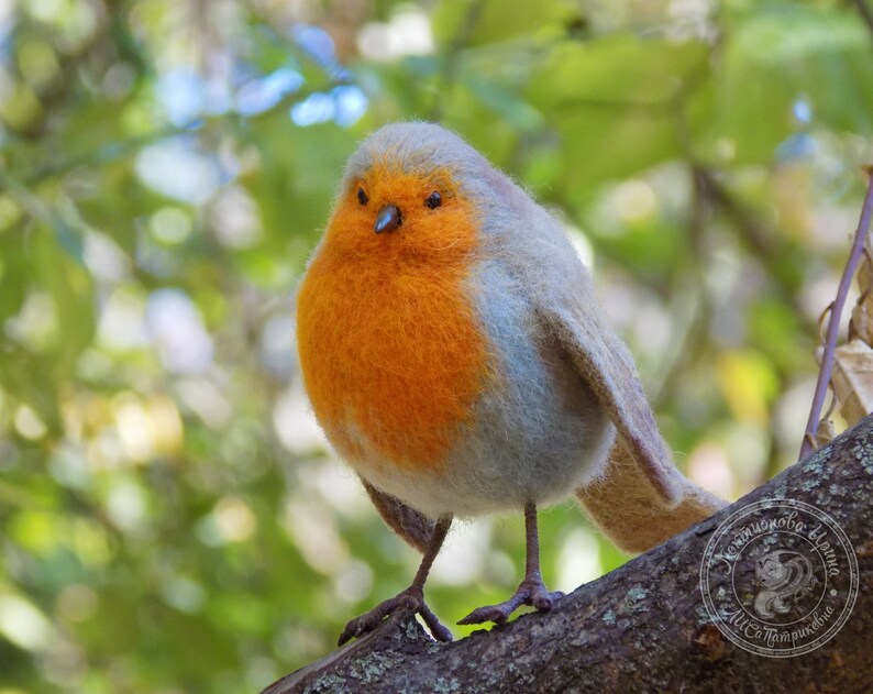 May include: A small, orange and gray felt bird with a black eye, perched on a branch. The bird is a robin, a common songbird.