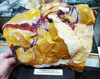 May include: A large, rough-hewn Australian Red/Yellow Mookaite Jasper stone. The stone features a mix of yellow, red, and white colors. The dimensions are 12" x 9.5" x 4.0" and weighs 19 lbs. The stone is from Mooka Creek, Kennedy Range, Western Australian.