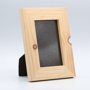 May include: A natural wood picture frame with a black backing and a stand. The frame is designed to hold a 10x15 cm photo.