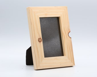 Op de afbeelding: Een fotolijst van natuurlijk hout met een zwarte achterkant en een standaard. De lijst is ontworpen om een foto van 10x15 cm te bevatten.