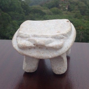 May include: A white ceramic sculpture of a four-legged animal with a rounded top. The sculpture is sitting on a dark brown wooden surface.