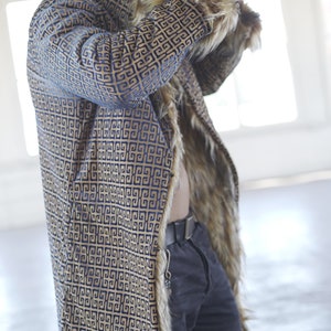 May include: A long, blue and gold patterned hooded coat with a fur trim. The coat has a geometric pattern and is lined with faux fur.
