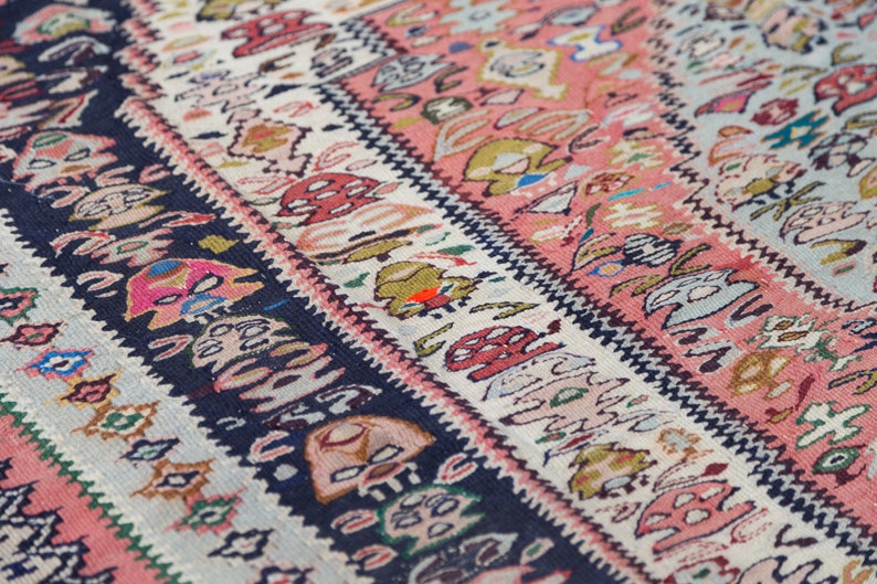 May include: Close-up of a colourful woven rug with intricate patterns in shades of pink, blue, green, and white.