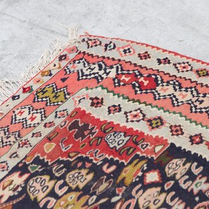 May include: Close-up of a colourful rug with intricate patterns in shades of red, black, white, and green. The rug has a fringed border and is folded in half.