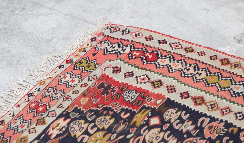 May include: Close-up of a colourful rug with intricate patterns in shades of red, black, white, and green. The rug has a fringed border and is folded in half.