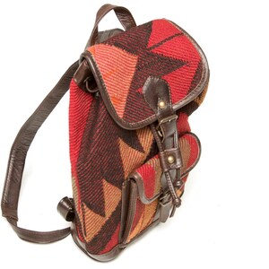 Può includere: Uno zaino piccolo con motivo rosso, marrone e arancione, con cinturini e fibbie in pelle marrone.