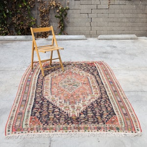 May include: A vintage rug with a dark blue background and a central medallion in shades of pink, cream, and ivory. The rug has a fringe border and intricate geometric patterns.