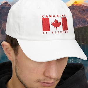 May include: White baseball cap with the Canadian flag and the text "CANADIAN BY DESCENT" in red. The cap has a curved peak and a classic six-panel design. The hat is made of a soft, durable material.