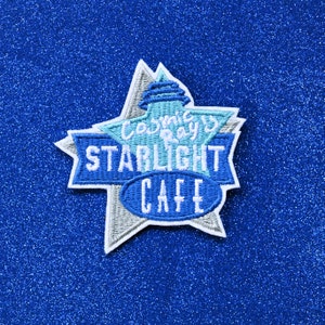 May include: A blue and white embroidered patch shaped like a star with the text "Cosmic Ray's Starlight Cafe" in white.