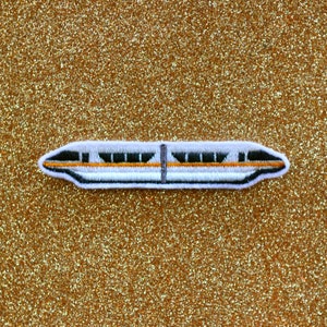 May include: White and black embroidered patch of a monorail train on a gold glitter background.