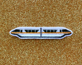 May include: White and black embroidered patch of a monorail train on a gold glitter background.
