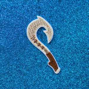 May include: A white and brown embroidered patch shaped like a traditional Hawaiian fish hook. The hook is decorated with a swirling pattern.