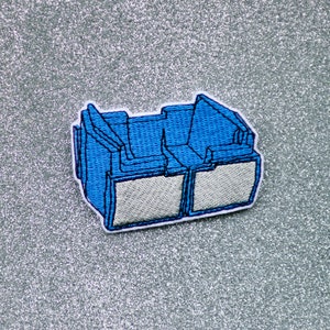 May include: A blue embroidered patch depicting a pair of 3D glasses. The glasses have a white frame and lenses.