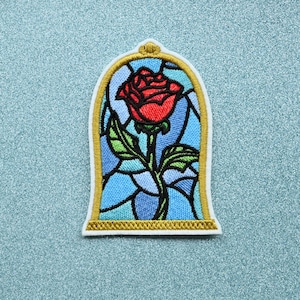 May include: Embroidered patch of a red rose in a stained glass window frame. The rose is surrounded by blue and green glass.