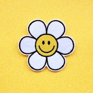 May include: A white flower with a yellow smiley face in the center. The flower is embroidered and has a black outline.